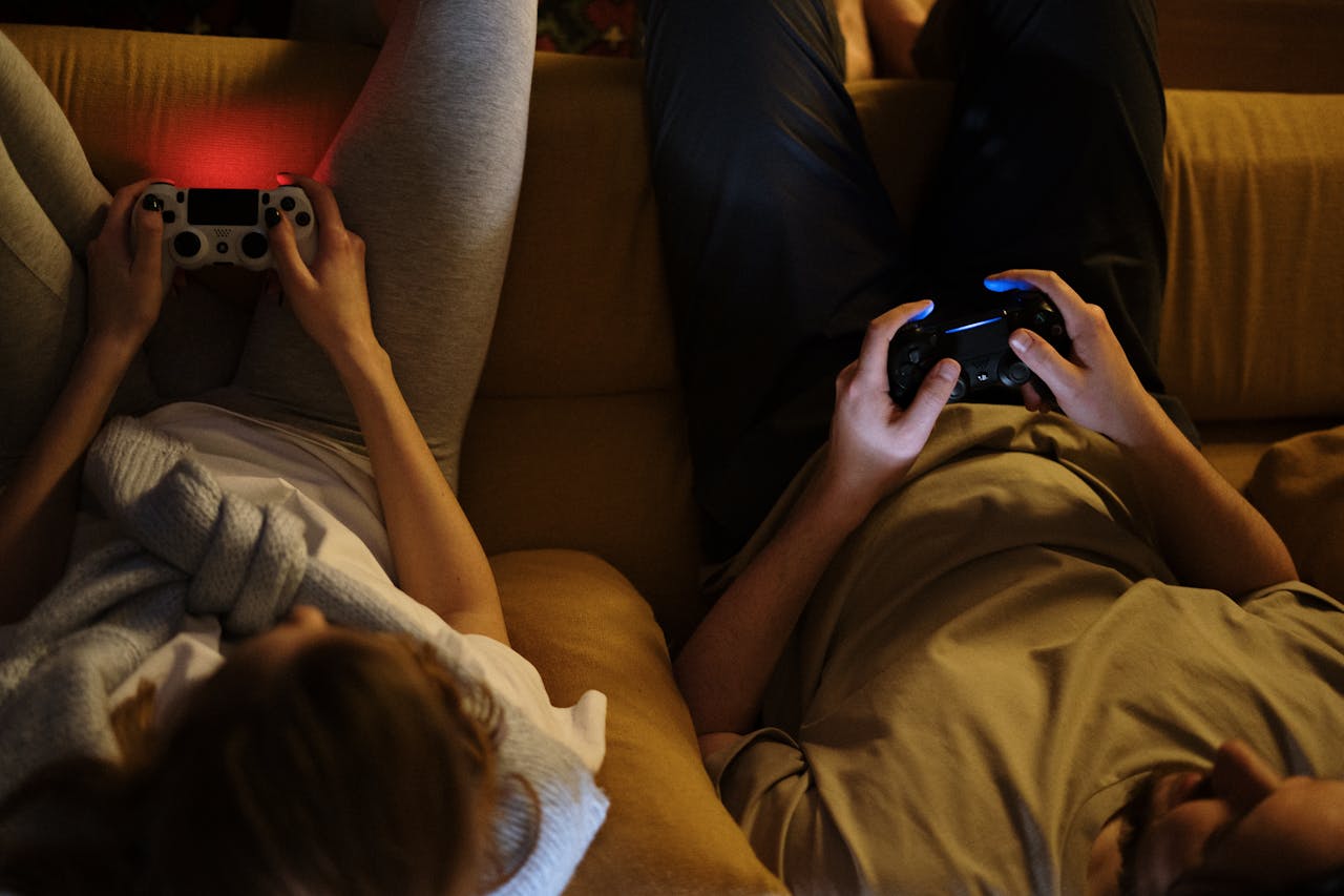 A couple enjoying an evening playing video games together on the sofa in cozy home lighting.