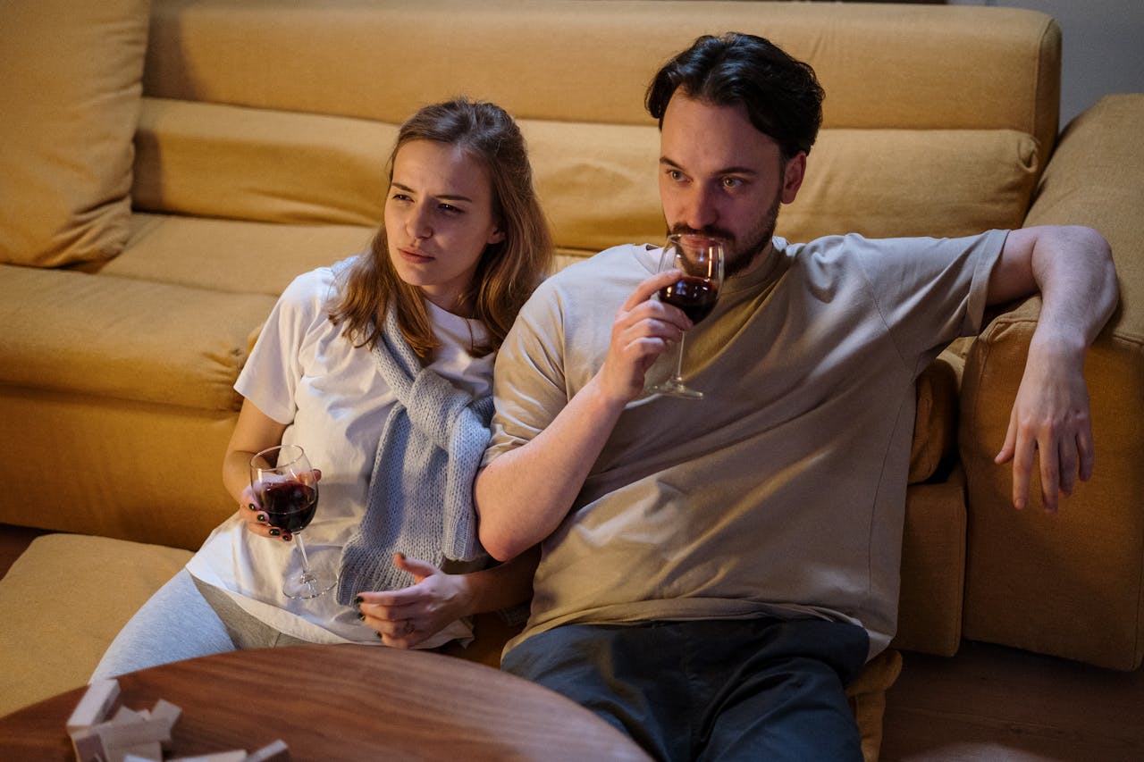 A couple sitting on a sofa at home, enjoying glasses of wine in a cozy setting.