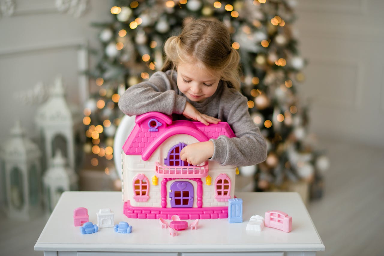 A young girl enjoys imaginative play with a pink dollhouse during the festive Christmas season.