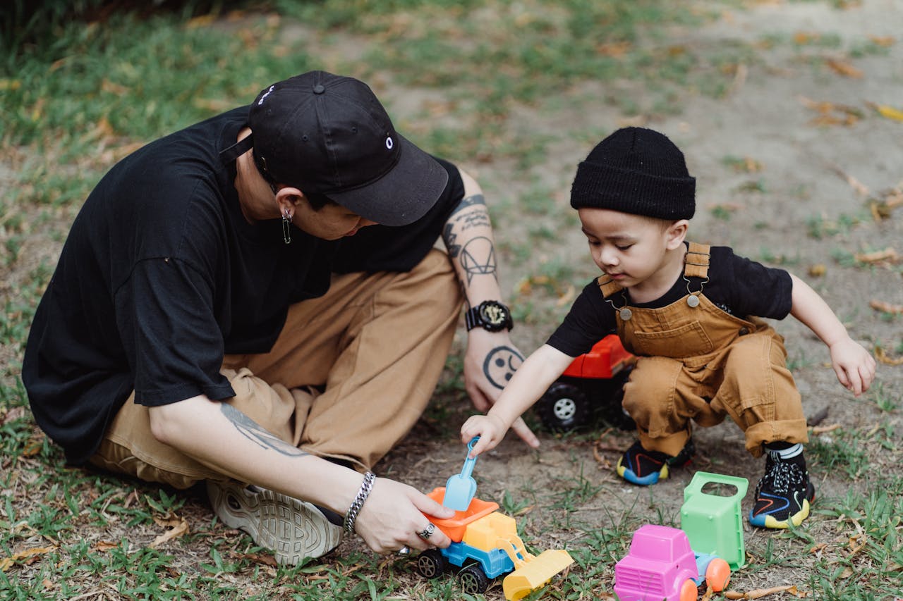 Father and son bonding outdoors, playing with toy cars. Casual and joyful family moment.