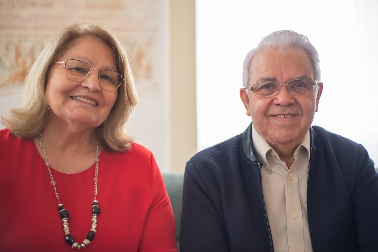 Elderly couple smiling and sitting together indoors, showcasing happiness and companionship.